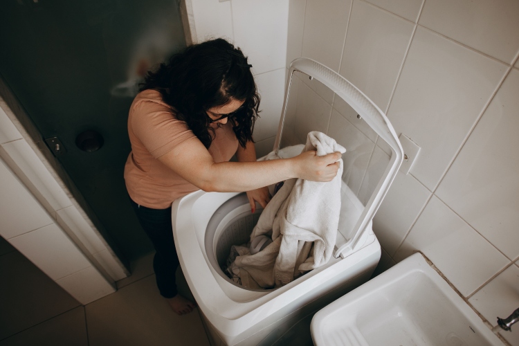 Persona utilizando una lavadora de alta eficiencia mientras selecciona un programa de lavado con agua fría para ahorrar energía en el hogar.