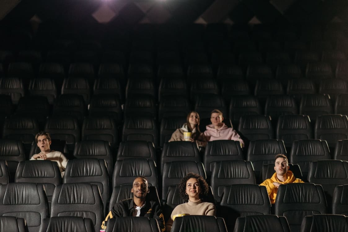 Personas observando el cartel de estrenos de cine en una sala de Cine Colombia antes de ingresar a una función de fin de semana.